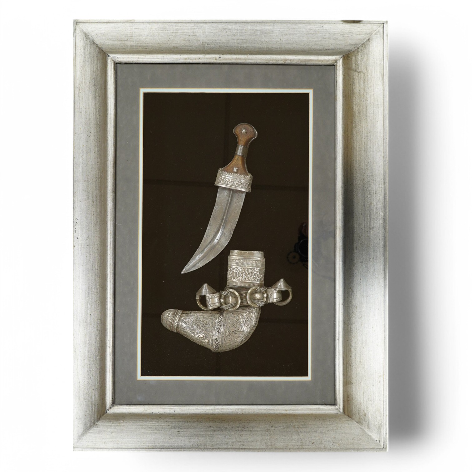 A silver mounted Arab Khanjar dagger from Oman, wooden grip, mounts chased in relief with scrolling foliage, contained in an illuminated display case for wall mounting, 79cm x 58.5cm. Condition - good.